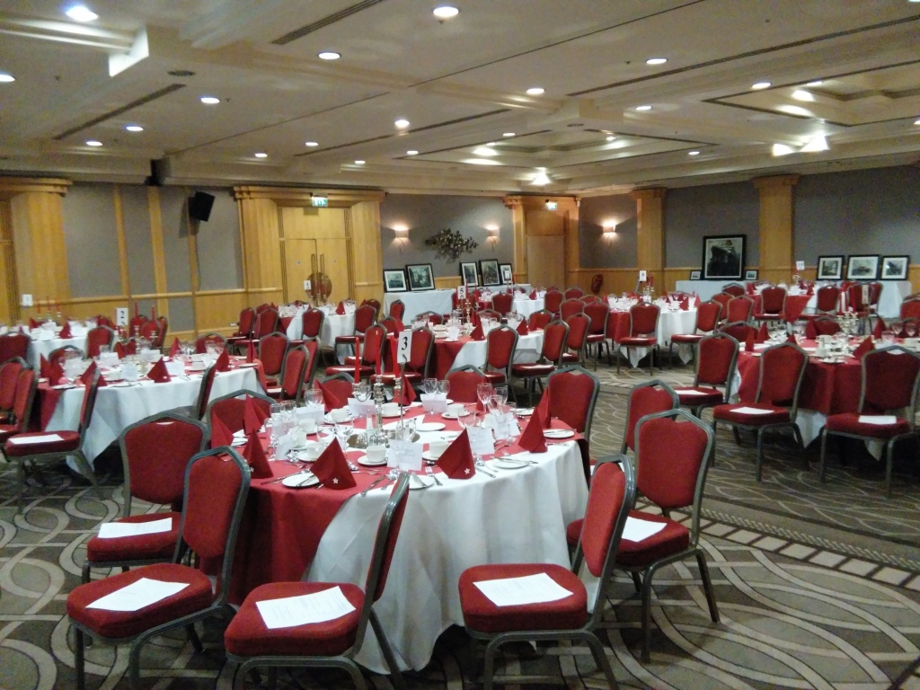 Image of room with tables set for dinner with white cloths, red runners and awhile star in the centre napkins also style in red with a white star.